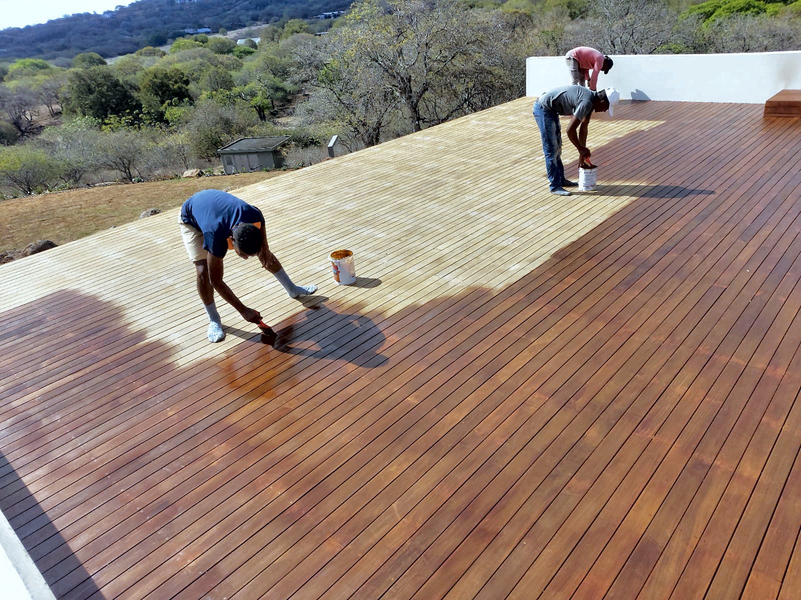 Équipe appliquant le saturateur sur une grande terrasse en bois poncée : avant et après