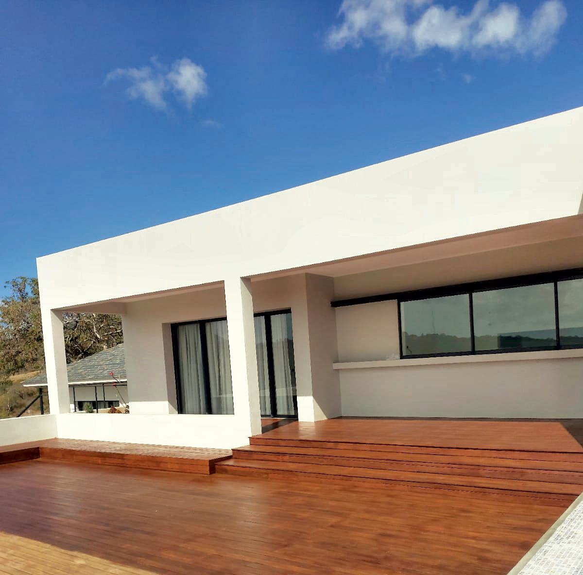 Villa contemporaine blanche et sa grande terrasse en bois exotique rénovée, sous un ciel bleu